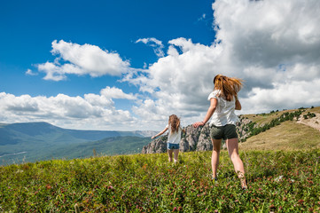 Two girls running on the meadow with mountains and cloudscape on background.