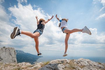 Two girls jumping on the cliff over the sea