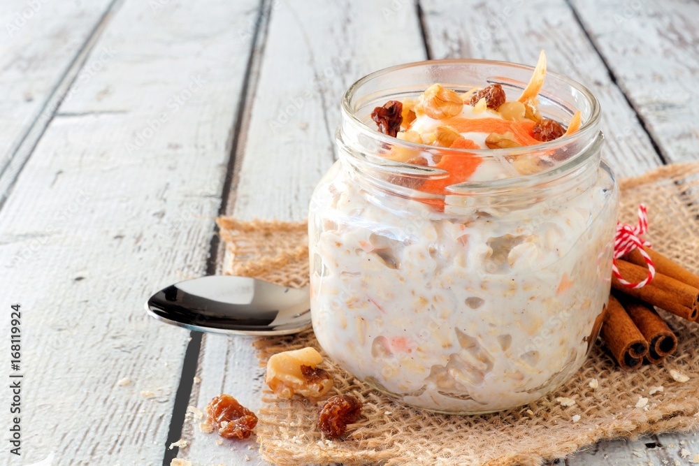 Wall mural carrot cake overnight oats with nuts and raisins in a mason jar on a rustic white wood background