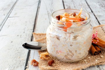 Carrot cake overnight oats with nuts and raisins in a mason jar on a rustic white wood background