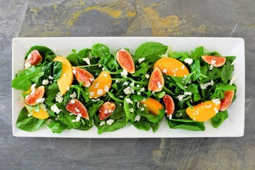 Autumn salad of arugula, spinach figs and goat cheese in a white rectangular plate, overhead view on slate