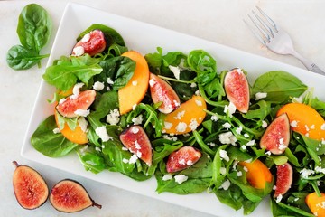 Autumn salad of arugula, spinach figs and goat cheese in a white rectangular plate, overhead scene on marble