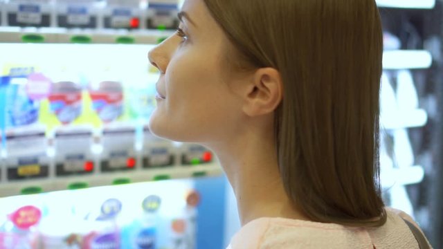 Beautiful hungry woman picking item out of vending machine in mall. Choosing unhealthy snacks being famished
