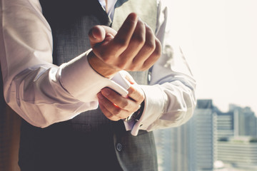Fototapeta premium A groom putting on cuff-links as he gets dressed in formal wear .Groom's suit