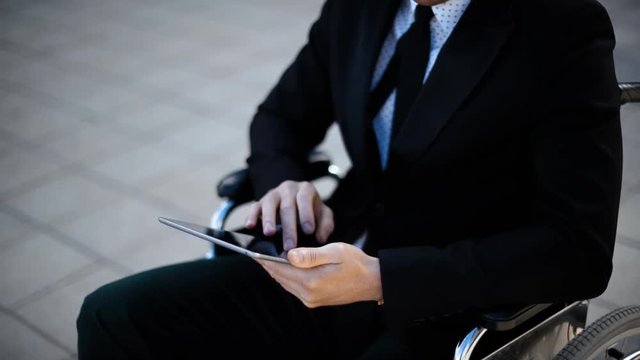 Young smiling handicapped Businessman sitting in wheelchair outdoor and work with digital pad outdoor