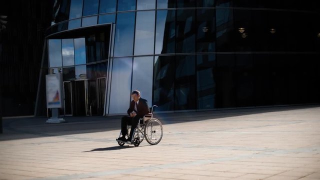 Sad handsome handicapped entrepreneur businessman in wheelchair whith indifferent crowd in business district and modern building teal orange.