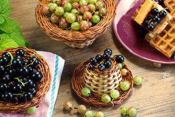 ягоды черная смородина крыжовник в плетеных корзинках  и бельгийские вафли на столе 