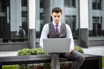 Young business school student working on a laptop computer while sitting on a bench