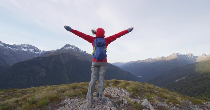 Success, achievement and winning concept with hiker cheering celebrating with arms outstretched against mountains at Routeburn track, Fiordland National Park, New, Zealand. SLOW MOTION.