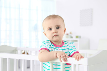 Cute little baby standing in crib at home