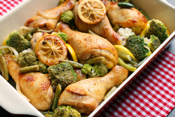 Baking dish with delicious roasted chicken drumsticks, lemon and vegetables on tablecloth