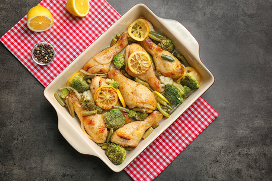 Delicious roasted chicken drumsticks with lemon and vegetables in baking dish on table