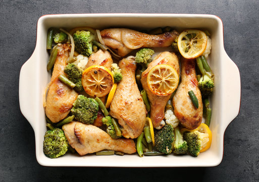 Delicious roasted chicken drumsticks with lemon and vegetables in baking dish on table