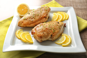 Plate with delicious roasted chicken and sliced lemon on wooden table