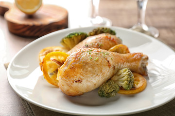 Plate with delicious roasted chicken drumsticks and lemon on table