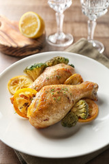 Plate with delicious roasted chicken drumsticks and lemon on served table