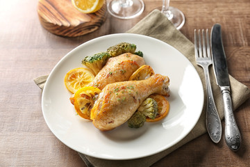Plate with delicious roasted chicken drumsticks and lemon on served table