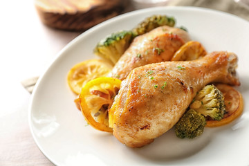 Delicious roasted chicken drumsticks with sliced lemon on plate