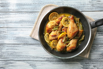 Delicious chicken drumsticks with lemon in frying pan on wooden table