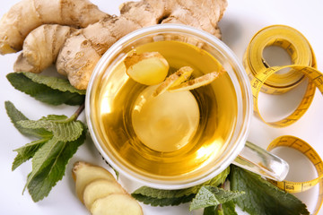 Composition with cup of tea, ginger, mint leaves and measuring tape on white background. Weight loss concept