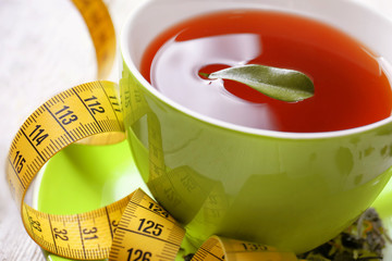 Closeup view of cup with tea, leaf and measuring tape on table. Weight loss concept