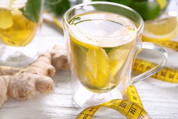 Cup with ginger tea and measuring tape on light table. Weight loss concept