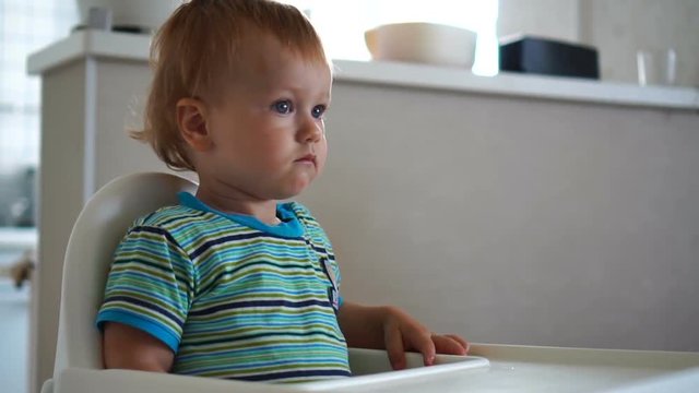 The little boy watches television carefully, sitting behind a child seat.