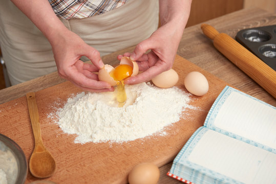 Woman preparing flour for baking on a wooden background. Raw food and kitchen utensils. Hands and food closeup. Break an egg, cooking dough.