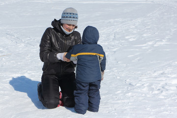 Woman correcting clothes to a child in the snow in winter