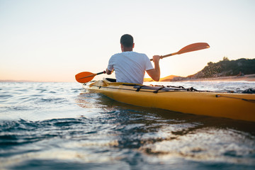 Man kayaker paddling the kayak at sunset sea
