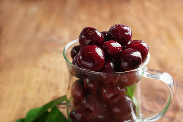 Glass cup with sweet cherries on wooden table