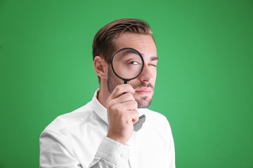 Handsome young man with magnifier on color background