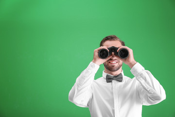Handsome young man with binocular on color background