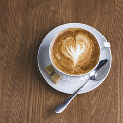 Cup of cappuccino with milk foam in heart shape on wooden background