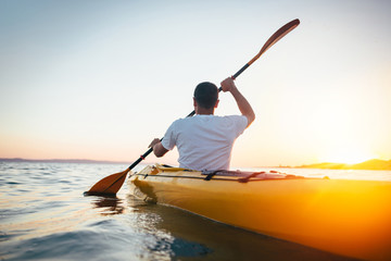 Rear view of man paddling canoe - obrazy, fototapety, plakaty