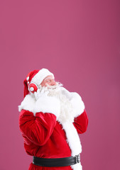 Santa Claus listening to music on color background