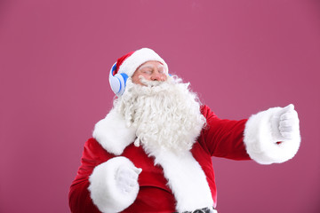 Fototapeta na wymiar Santa Claus listening to music on color background