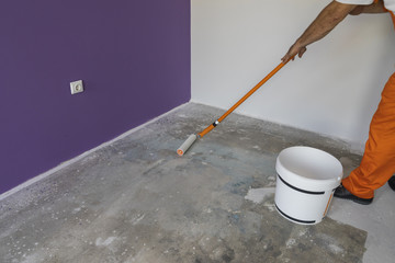 The hand of a man holding a roller and puts primer on cement flo