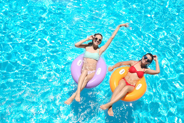 Beautiful young women with inflatable rings in blue swimming pool