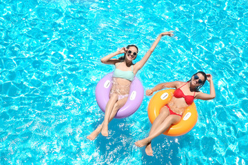 Obraz premium Beautiful young women with inflatable rings in blue swimming pool