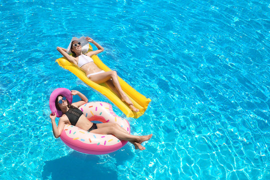 Beautiful young women with inflatable donut and mattress in blue swimming pool