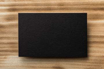 Closeup mockup of black blank horizontal business card at natural wooden background.