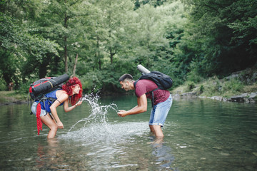 Happy young hikers couple enjoying in adventure. They camping and having fun while walking through the wild mountain river.