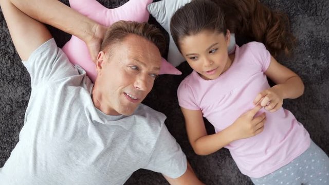 Cheerful man and his little daughter resting on the floor at home
