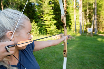 Female Archer Aiming Arrow At Target Board In Forest