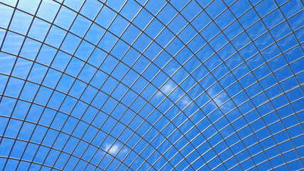 A dome shaped glass ceiling with metal support structure beams or frame with blue sky and a little white clouds in the background.