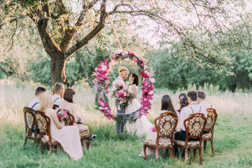 The beautiful wedding ceremony in the sunny park. The horizontal photo of the newlyweds with...