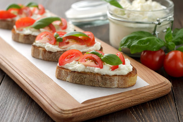Bruschetta with cheese feta, tomatoes and basil on wooden cuttin board.