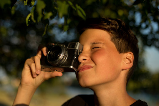 Young photographer with retro film photo camera in garden. The boy holds a camera in his hands and takes pictures of trees