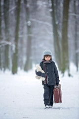 Fototapeta na wymiar Sad child, boy, walking in a forest with old suitcase and teddy bear